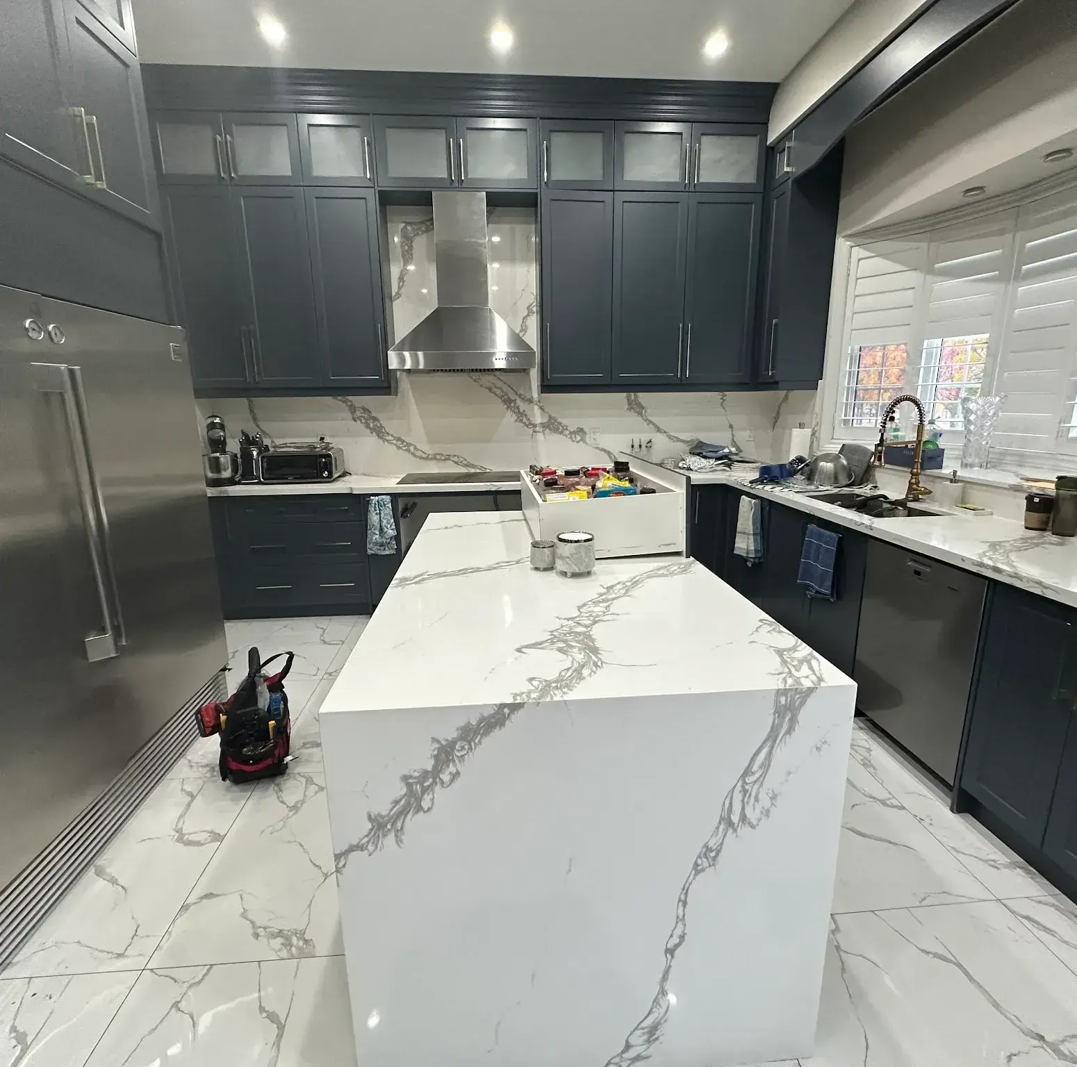 Navy shaker kitchen with waterfall quartz island, mid-install