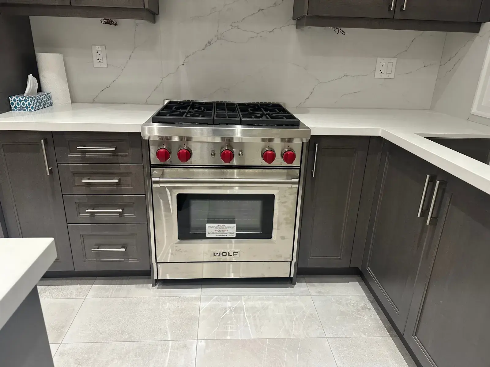 Wolf range with red knobs installed against a white quartz and marble backsplash