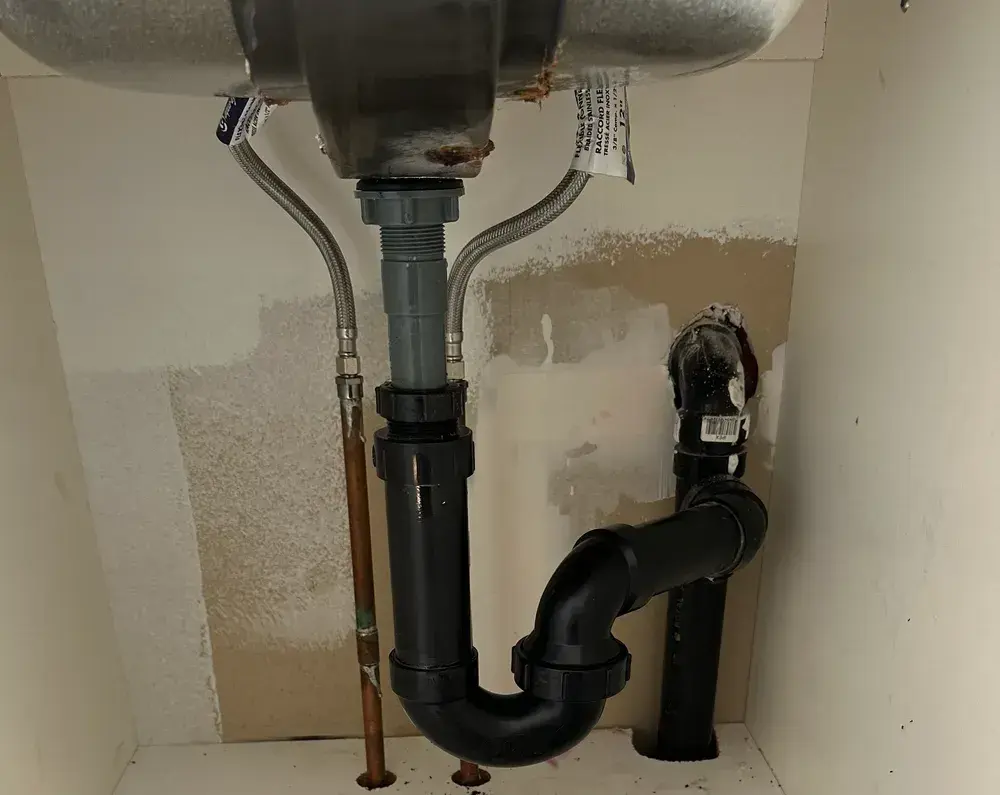 Under-sink cabinet mid-repair, old drain trap disassembled, new tailpiece hanging from the sink flange