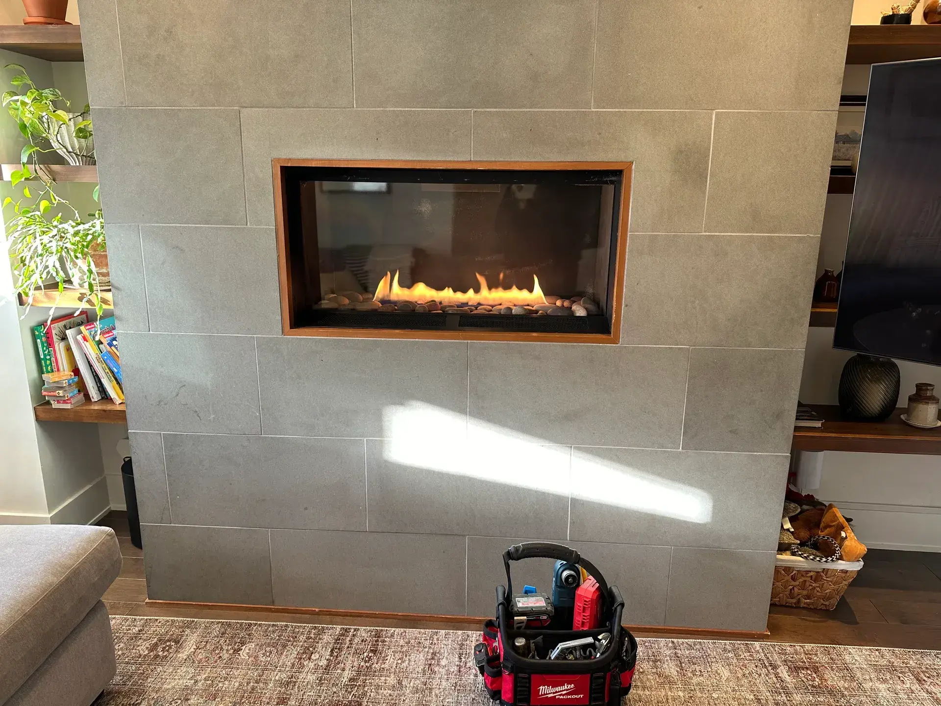 Modern linear gas fireplace burning in a grey tile feature wall during a service call