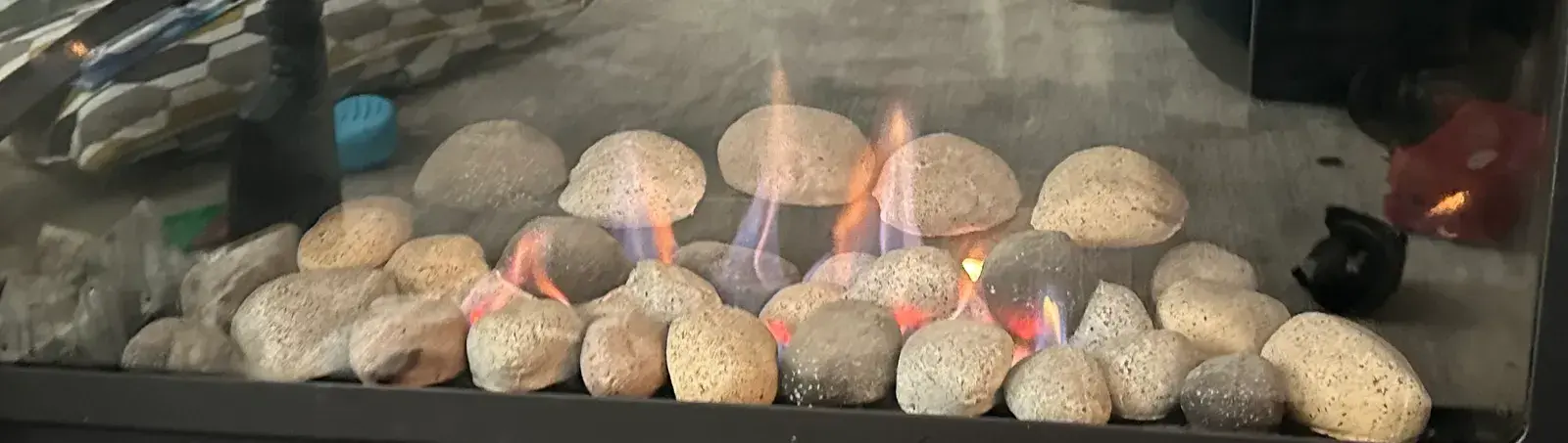 Blue and orange flames over stones inside a gas fireplace during a service call