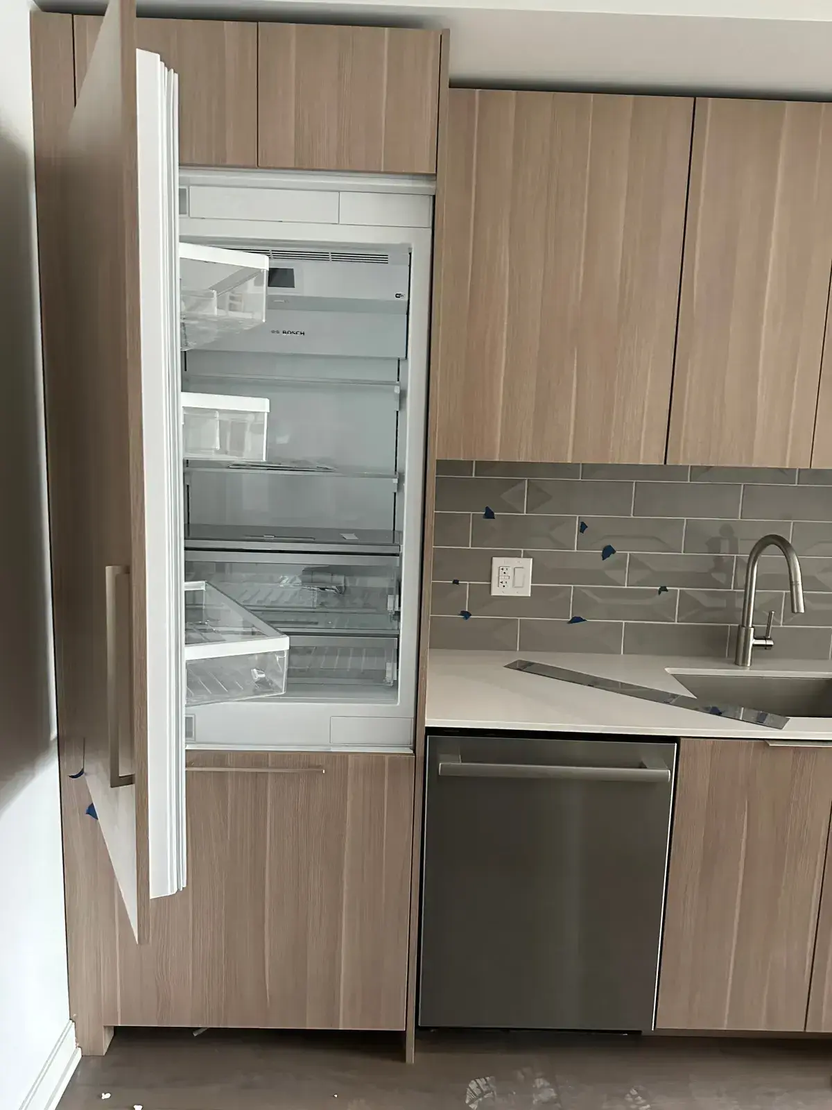 Newly installed refrigerator with the door open, set into wood cabinetry