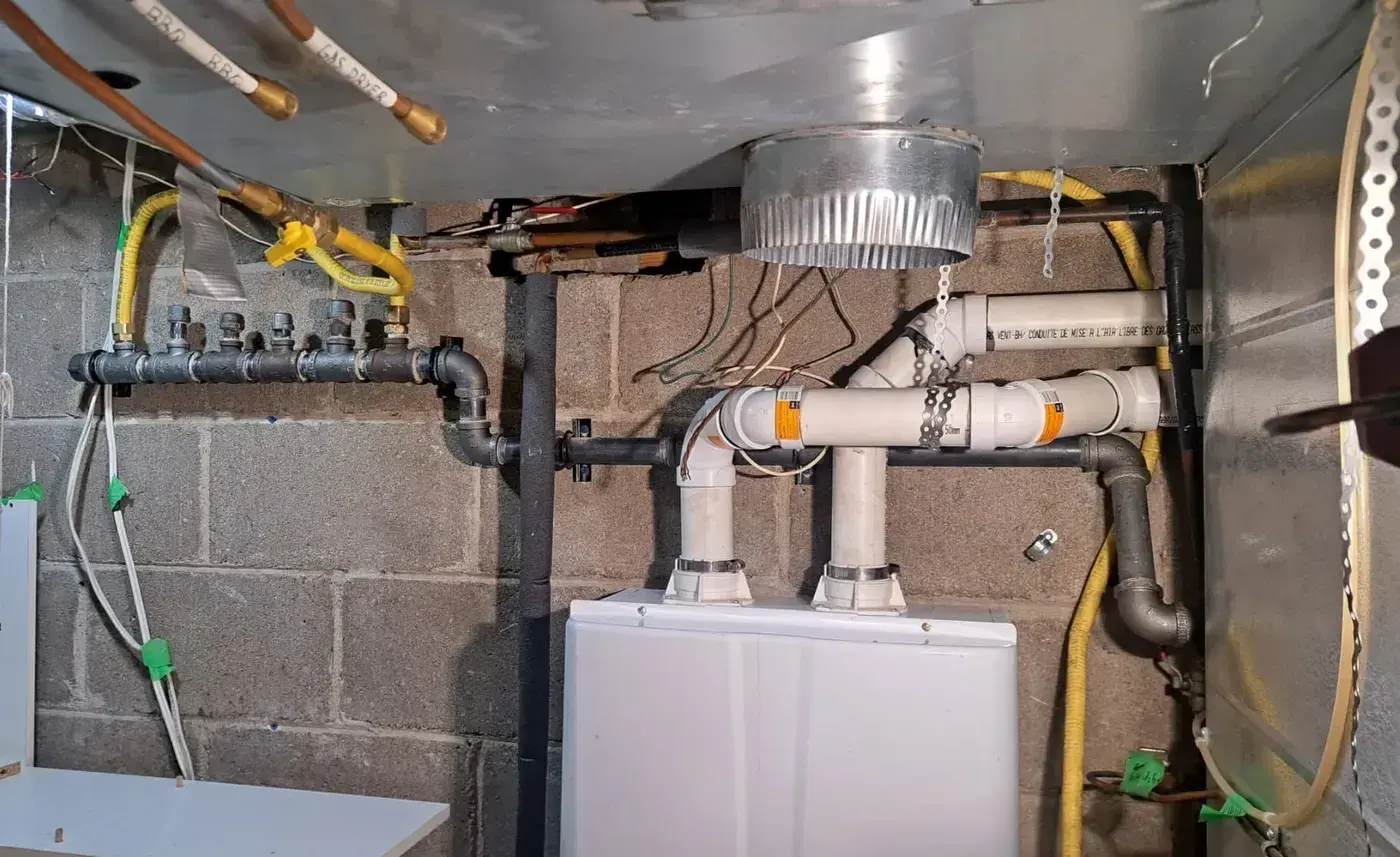 Black-iron gas manifold with labelled copper drops and a tankless water heater beside it