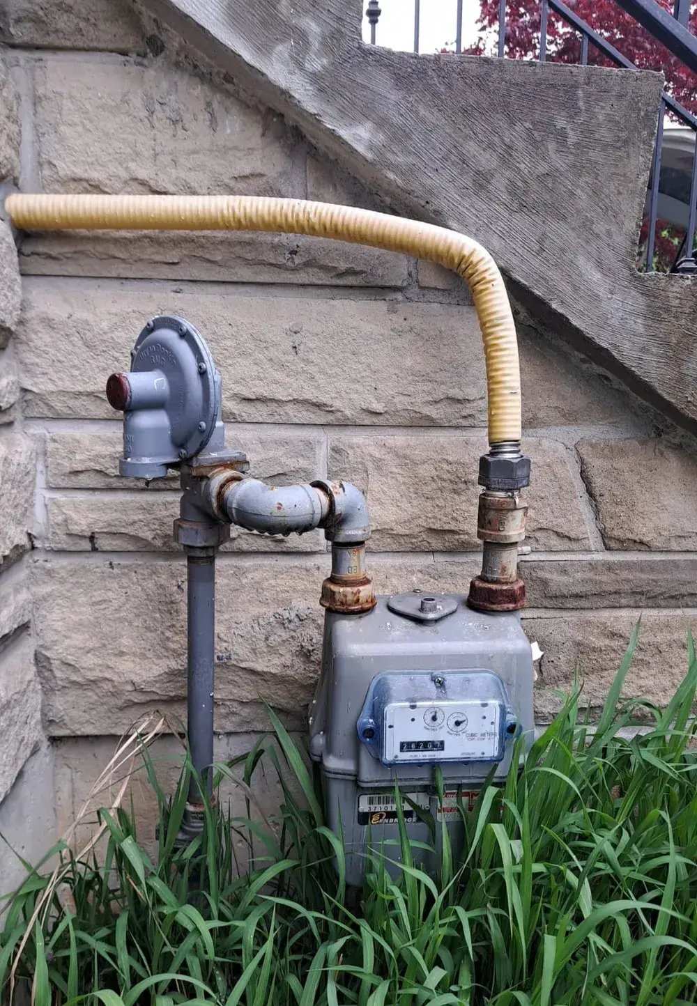 Gas meter with rusted unions and an old yellow corrugated flex line on a stone wall