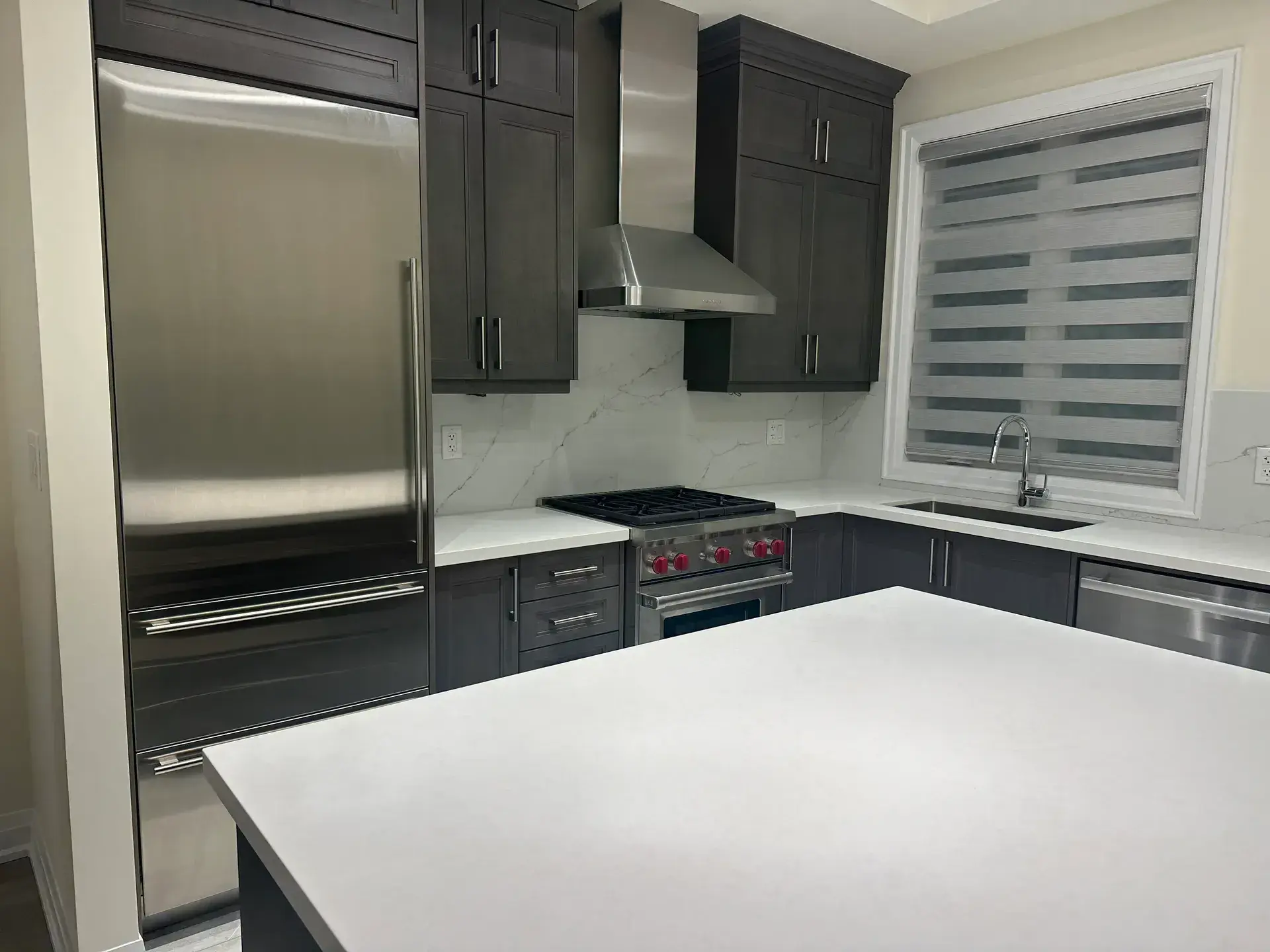 Finished grey kitchen with built-in refrigerator column, Wolf range with red knobs and chimney hood