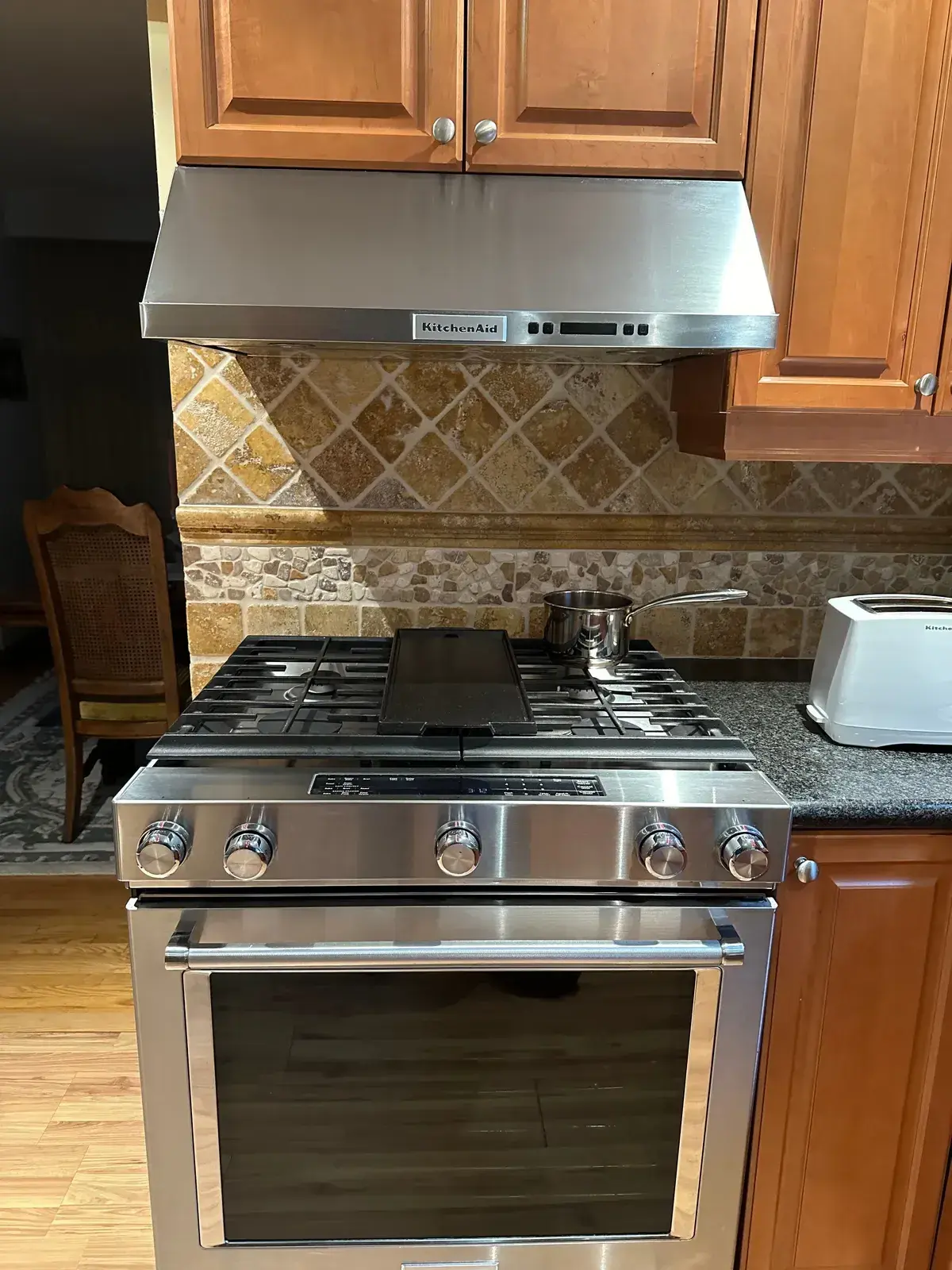 Stainless gas range and chimney hood against a travertine backsplash